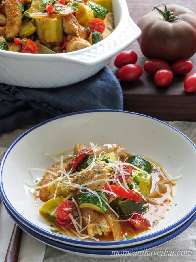 A bowl of chicken and summer vegetables sauteed in a flavorful sauce and topped with Parmesan cheese and chopped parsley.