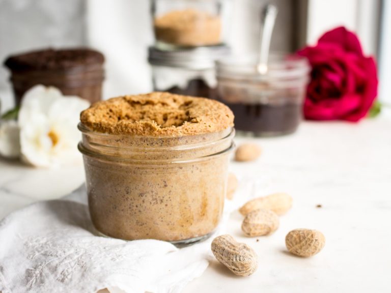 keto peanut butter mug cake in a jar with peanuts and chocolate peanut butter mug cakes behind