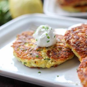 Zucchini fritter with sour cream and chives on a white plate.