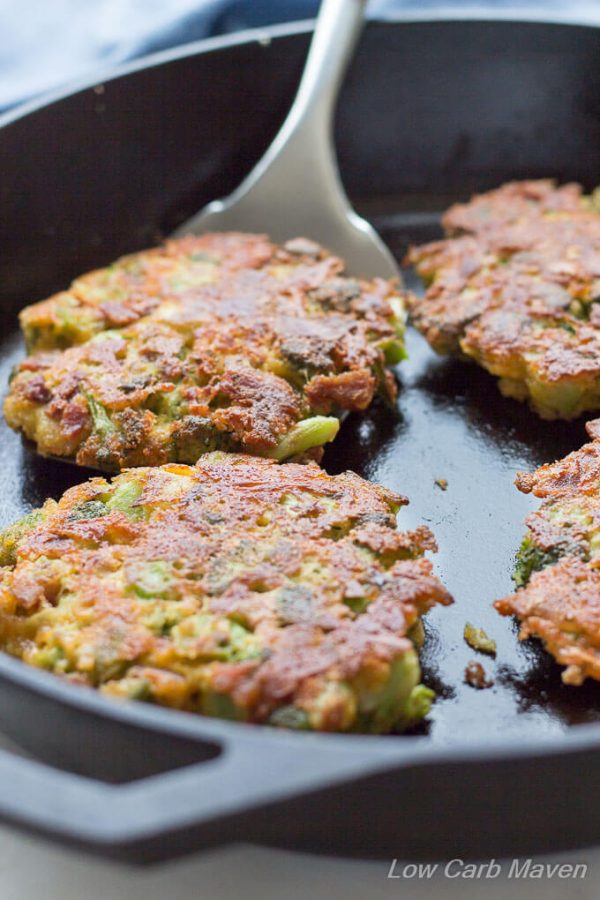 Crusty and browned broccoli fritters with cheddar cheese in a cast iron pan with a spatula positioned under a fritter patty ready to lift it out of the pan.