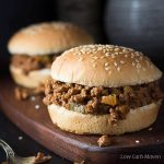 homemade sloppy joes recipe with onions and bell peppers in the sauce on sesame seed buns on a cutting board.
