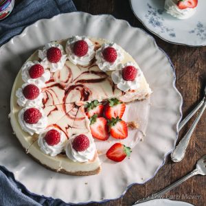 Strawberry and raspberry swirl cheesecake with whipped cream, fresh raspberries and strawberries on a plate.