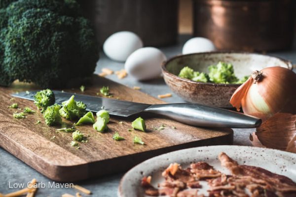 Ingredients for cheddar broccoli quiche: chopped broccoli on a cutting board, eggs, and bacon.