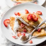Folded Keto strawberry crepes and whipped cream on a plate with napkin.