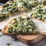 Slices of spinach artichoke pizza on cutting board.