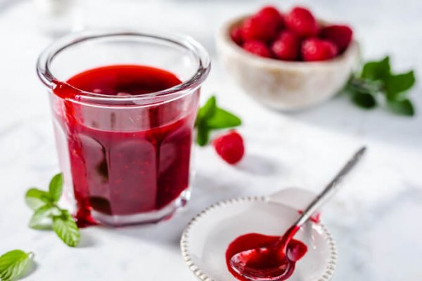 Raspberry sauce in a jar with fresh raspberries, mint, and a spoon.