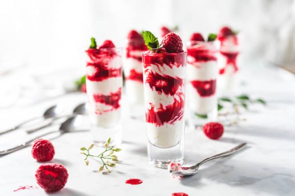 Keto raspberry sauce and cheesecake fluff layered in shot glasses like a parfait and topped with raspberries and mint.