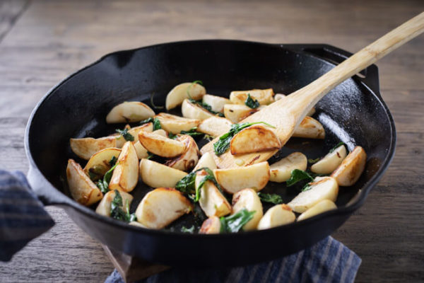 Cooked pan fried turnips in a pan with spinach and a bamboo spatula