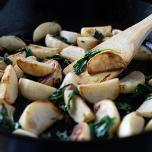 Pan fried turnips in a cast iron pan with wooden spatula