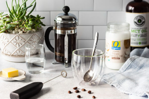 Ingredients for Keto coffee: grass-fed butter, coffee, coconut oil, MCT oil with French press, milk frother and coffee cup