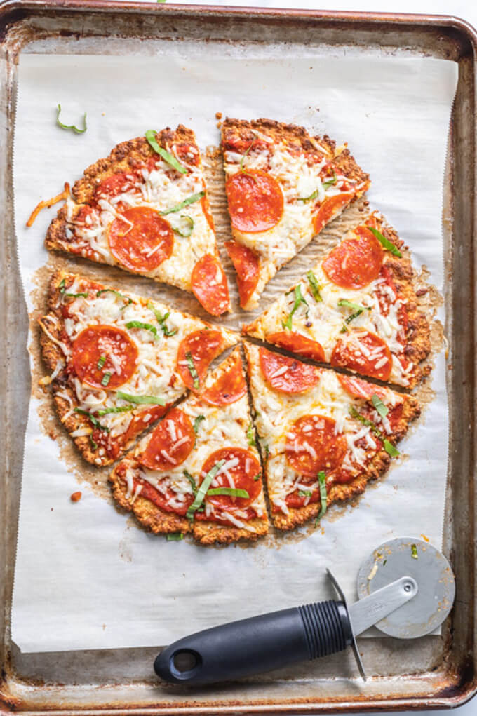 cauliflower pizza crust pizza with pizza cutter on a sheet pan