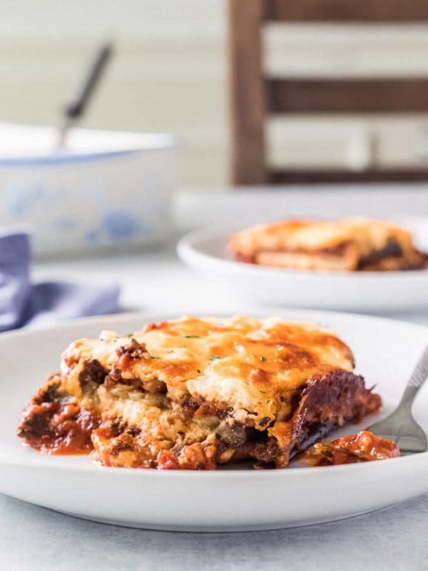 Plates of keto eggplant lasagna with forks on a table with lasagna pan and chair in background