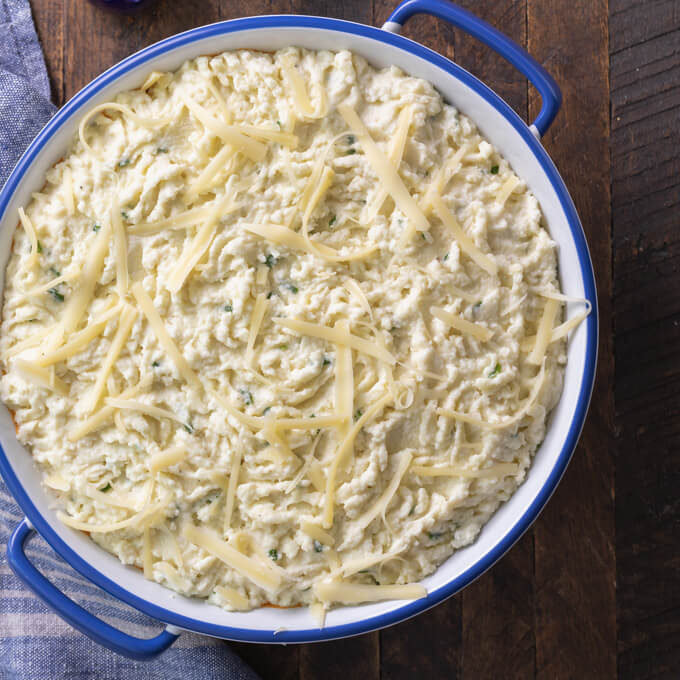 Unbaked Cottage Pie with mashed cauliflower and cheese on top in a blue rimmed casserole dish with blue napkin to the side.