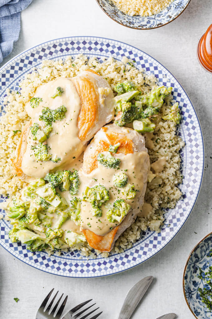 Keto Chicken Broccoli Alfredo over cauliflower rice on a plate with napkin and fork and knife.