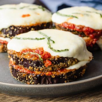 Stacks of keto eggplant parmesan rounds with marinara sauce and melted mozzarella cheese topped with basil